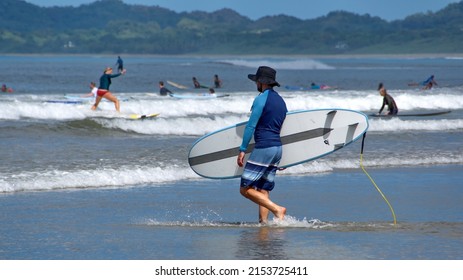 TAMARINDO, COSTA RICA - CIRCA NOVEMBER 2021: Person Walking On The Beach With A Surf Board