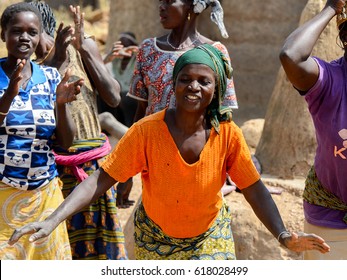 TAMBERMA VIL, TOGO - JAN 13, 2017: Unidentified Tammari A Woman In An Orange T-shirt Dances Near The Girls Who Clap Their Hands In The Village. Tammaris Are Ethnic Group Of Togo And Benin