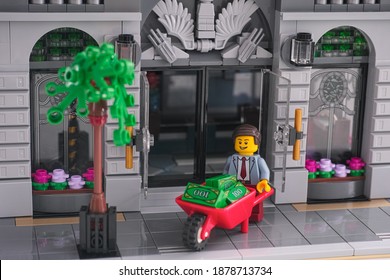 Tambov, Russian Federation - December 19, 2020 Lego businessman using a wheelbarrow to transport money in front of a bank. Studio shot. 