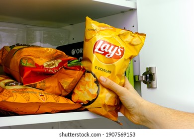 Tambov, Russian Federation - January 25, 2021 Woman Hand Taking Lays Potato Chips Bag Out Of A Cupboard With Other Snack