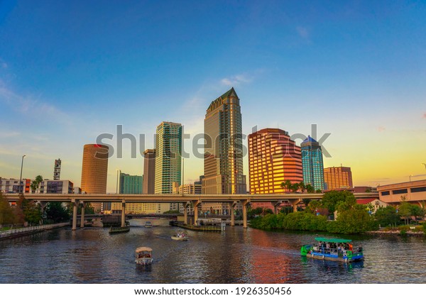 Tampa, Florida, USA - January 12, 2020 : The\
skyline of downtown Tampa at sunset with tourist boats on the\
Hillsborough river.
