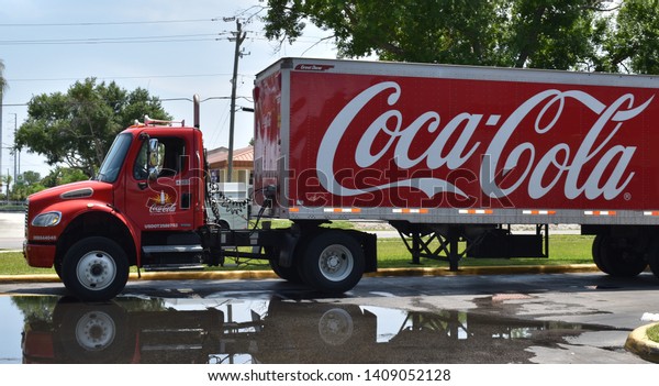 Tampa, Florida / USA - May 15th\
2019: Clean, shiny red and white iconic Coca Cola delivery truck on\
parking lot in the afternoon sun after a summer rain\
shower
