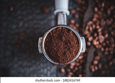 Tamped puck of coffee grounds within basket of portafilter and coffee beans spilled around in a dark and moody scene of natural light. - Powered by Shutterstock