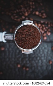 Tamped Puck Of Coffee Grounds Within Basket Of Portafilter And Coffee Beans Spilled Around In A Dark And Moody Scene Of Natural Light.