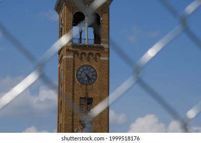 A Tan Brick Clock Tower As Seen Through A Metal Fence