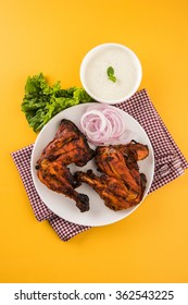 Tandoori chicken - prepared by roasting chicken marinated in yoghurt and spices in a tandoor. Leg piece served in a plate with salad over colourful or wooden background. Selective focus