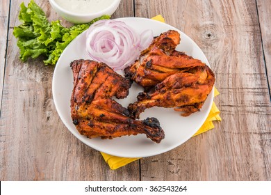 Tandoori chicken - prepared by roasting chicken marinated in yoghurt and spices in a tandoor. Leg piece served in a plate with salad over colourful or wooden background. Selective focus