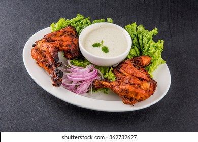 Tandoori chicken - prepared by roasting chicken marinated in yoghurt and spices in a tandoor. Leg pieces served in a plate with salad and chutney over colourful or wooden background. Selective focus