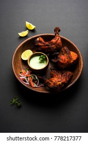Tandoori chicken - prepared by roasting chicken marinated in yoghurt and spices in a tandoor. Leg pieces served in a plate with salad & chutney over colourful or wooden background. Selective focus