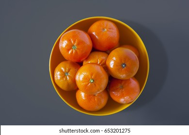 Tangerines, Clementines, In A Yellow Plastic Bowl On A Grey Background, Overhead Perspective.