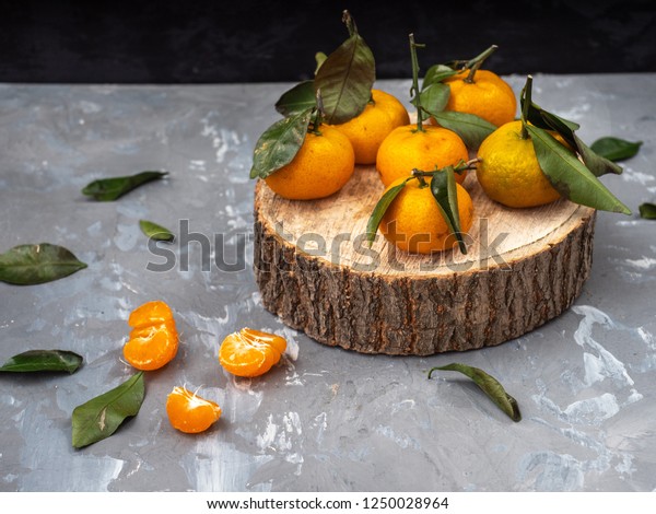 tangerines with\
leaves on a wooden disk, cleaned tangerine. Green leaves nazbrosany\
around on a gray\
background