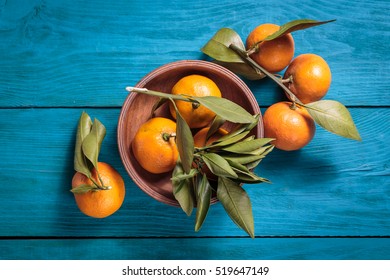 Tangerines with leaves in a wooden bowl on blue background. Top view.