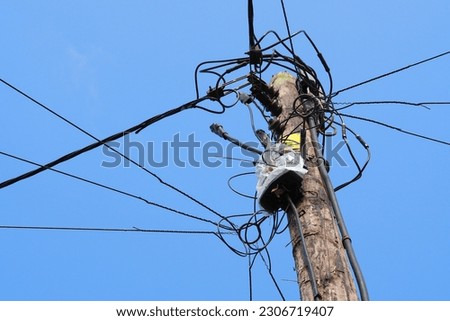 Tangled cable lines on wooden pole against blue sky with space for runaround or wraparound text 