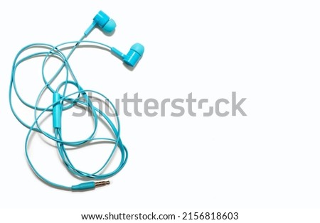 Tangled headphones lie on a white background. Blue headphones are twisted and untangling them is a big problem. Portable blue headphones with knots on an isolated white background. Free space for text
