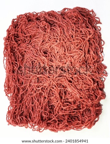 A lot of tangled thread. Red fabric background. Cords for knitting clothes, sewing factory. Soft threads for sewing. Red fluffy background. Thread for weaving.