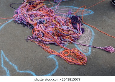 A tangled web of multi-colored knitting threads lies on the asphalt after a communication game.