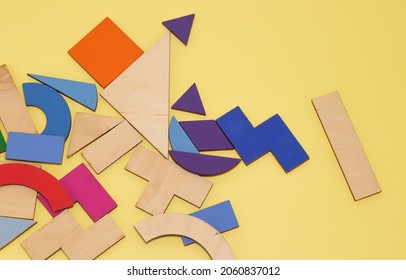 tangram game pieces placed chaotic on a wooden board. colorful puzzle pieces. green, violet, pink, orange. iq games, intelligence and educational jigsaw game