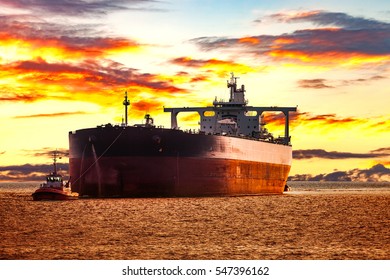 Tanker Ship With Escorting Tugboat On Sea At Sunrise.