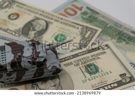 Tanks are placed on top of dollar bills. A metaphor for currency warfare, financial crises, trade wars, tariff penalties, international competition, war costs, and military spending.