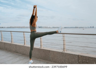 tanned American girl in sports clothes training on the oceanfront stretches her muscles before running. The road is a way of life. Fit woman trains outdoors - Powered by Shutterstock