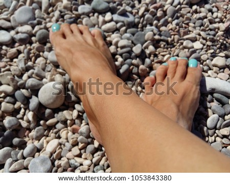 tanned female crossed legs on a pebble beach