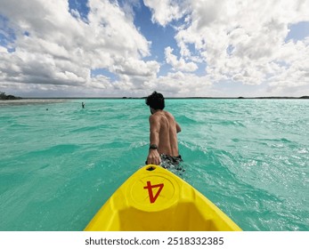 Tanned fit guy pulling a rented yellow kayak in clear light blue water. Cloudy sky. Bacalar lagoon. Quintana Roo. Mexico. Garmin watch on wrist. 