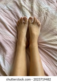 Tanned Legs. The Body Is On The Bed. Pink Sheet. Female Figure.