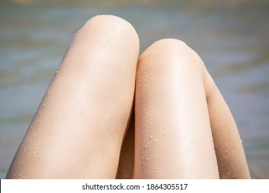 Tanned legs of girl with drops on the seashore