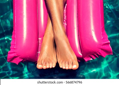 Tanned well-groomed feet in the pool on magenta  inflatable mattress for swimming . Pedicure and foot Spa . Manicured nails on the feet . Foot massage - Powered by Shutterstock