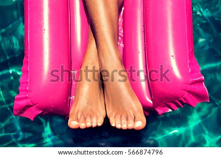Tanned well-groomed feet in the pool on magenta  inflatable mattress for swimming . Pedicure and foot Spa . Manicured nails on the feet . Foot massage