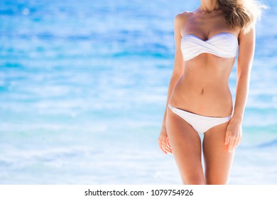 Tanned woman body in white bikini, blue sea water in background