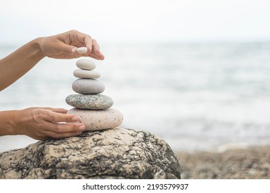 Tanned woman hands stacked pebble stones tower on sea beach relaxing harmony summer travel vacation. Female arms pillar formation peaceful balance pyramid spa spiritual gravel cobblestone at seaside