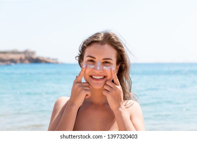 Tanned Woman Protects Her Face With Sun Cream From Sunburn At The Beach.