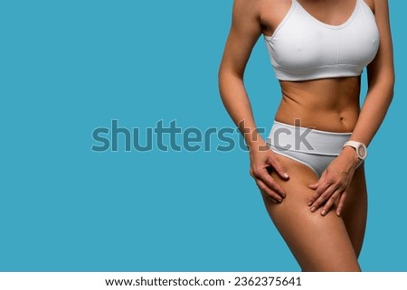 Tanned woman in white comfortable underwear compressing skin on hips checking for cellulite and excess subcutaneous fat. Copy space blue background