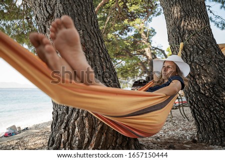 Tanned young woman relaxing in a hammock hanging between trees by the beach.