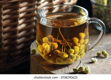 Tansy seed tea or infusion in a glass cup with flowers on wood with books nearby, herbal drink is good as anthelmintic, menstrual, kidney, rheumatism remedy , closeup, naturopathy, homeopathy concept - Shutterstock ID 1938290623
