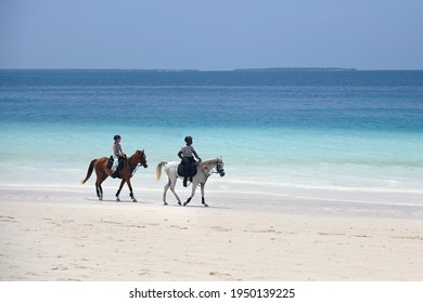 Tanzania, Zanzibar, 19.11.2020 A young girl takes horse riding lessons from an adult teacher. A white-skinned girl and a dark-skinned man ride a horse on a white beach. orse riding on a sunny day.