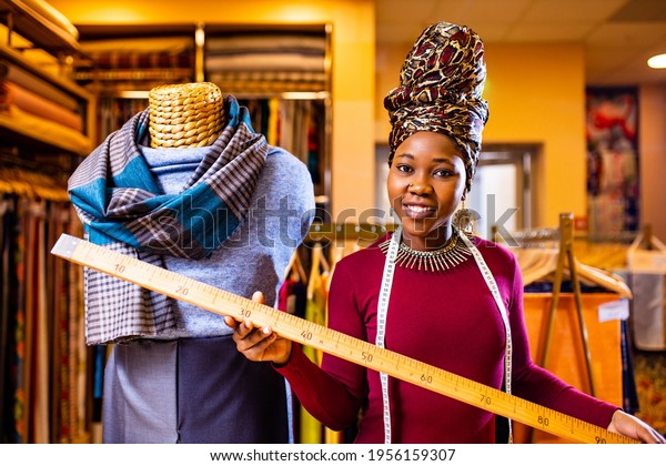 tanzanian woman with snake print turban over\
hear working in fabrics shop with\
ruler