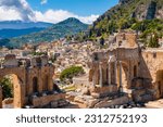 Taormina on Sicily, Italy. Ruins of ancient Greek theater, mount Etna covered with clouds. Taormina old town and mountains in background. Popular touristic destination on Sicily