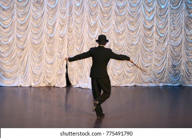 Tap dance with a cane in a black hat. Dance step. A man is dancing on stage