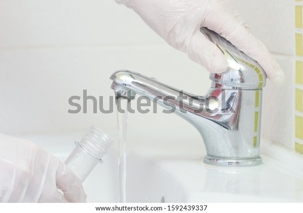 Tap water analysis quality control concept.\
Hand with a flask and water tap ckose\
up.