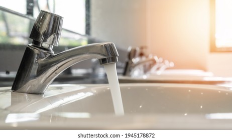 Tap water running wastage from faucet over hand washing sink, ceramic basin in water closet, public wc room or school bathroom for saving ecological and environmental conservation awareness concept