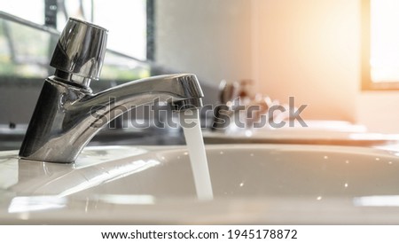Tap water running wastage from faucet over hand washing sink, ceramic basin in water closet, public wc room or school bathroom for saving ecological and environmental conservation awareness concept