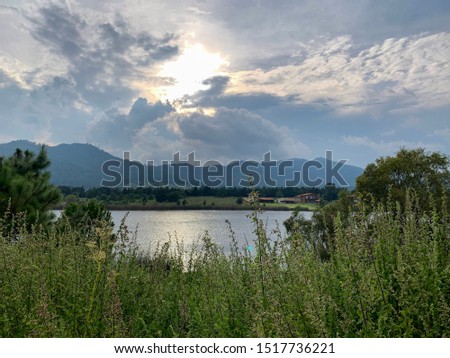 Tapalpa valley with views of the lake, fields and meadows. Coudy sky with sunlight forming half a cirlcle. Sierra landscape