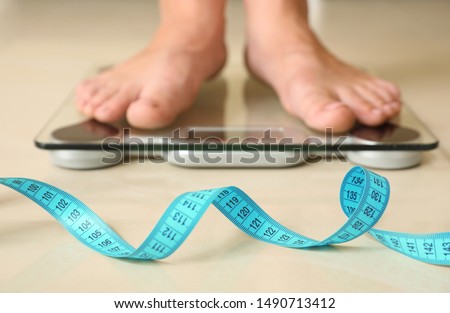 Tape in front of woman standing on floor scales indoors. Overweight problem
