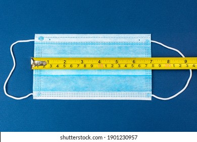 Tape Measure Ruler On Medical Mask With Blue Background. The Concept Of Sewing Masks At The Factory. Measuring The Face Mask