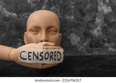 Taped wooden hand with word CENSORED and human head on dark table