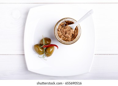 Tapenade - spicy olive paste made from green olives and red hot chili pepper in glass jar on white wooden table. 