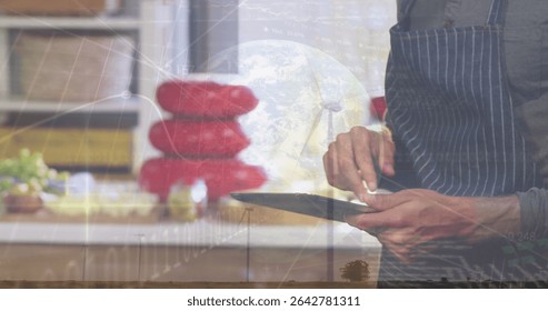 Tapping stylus on tablet while chef wearing apron at kitchen counter, with globe overlay. Technology, innovation, culinary, modern, digital, professional, touchscreen