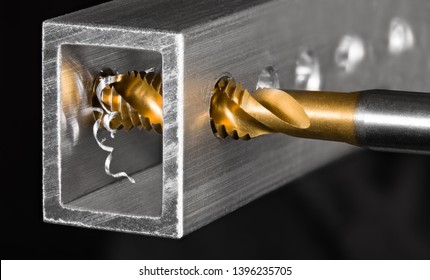 Tapping tool. Steel tap drill coated by titanium. Spiral swarf. Cutting of thread in hole. Aluminum alloy profile. Working cutter. Abstract chip machining detail on black background. Metal production. - Shutterstock ID 1396235705